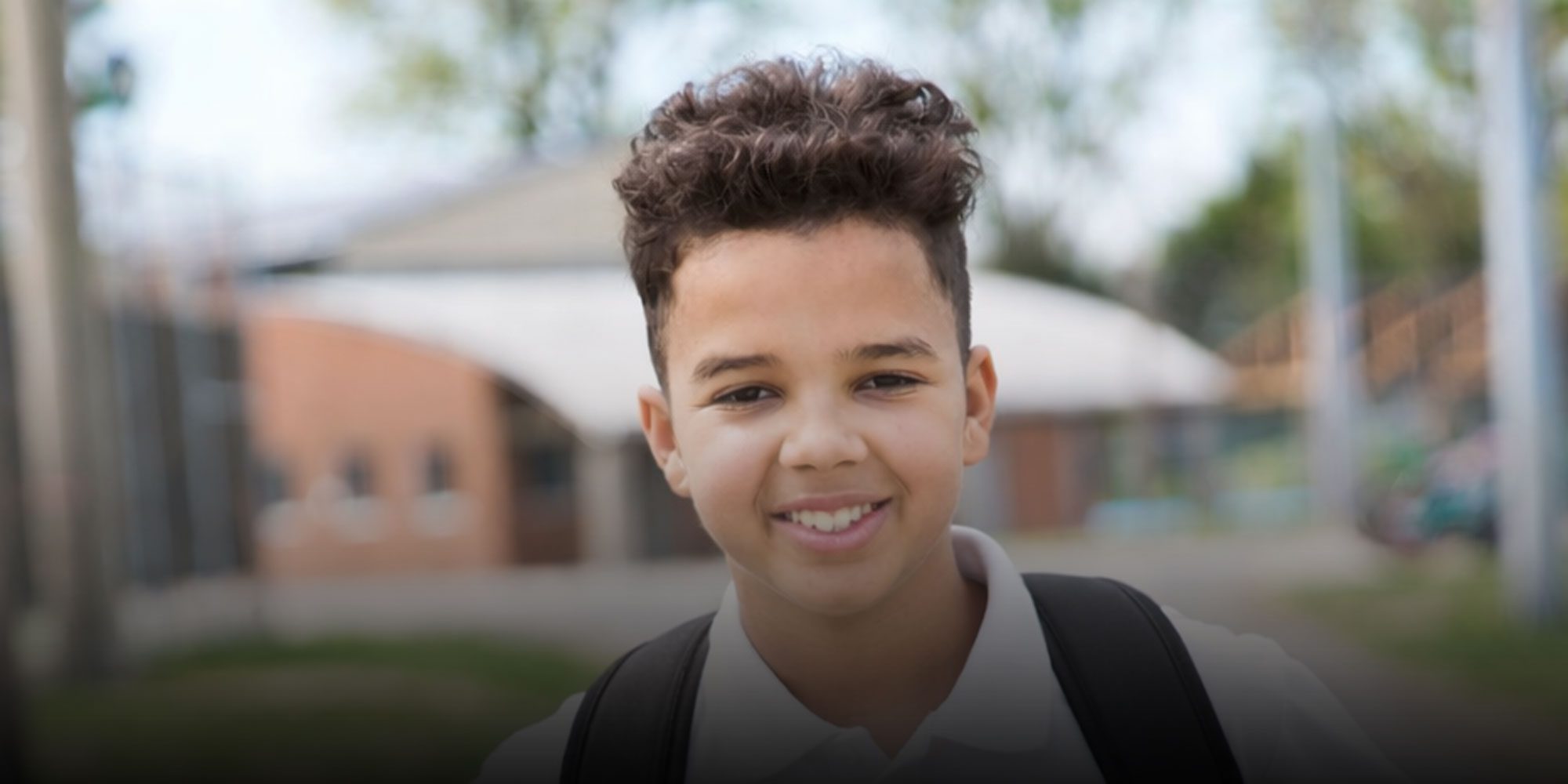 Smiling student with a backpack standing outside school.